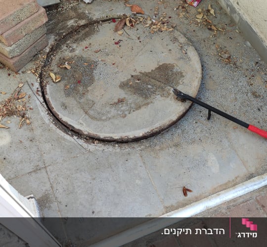 מכסה ביוב עם מוט פתיחה על רצפה מלוכלכת